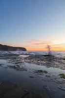 olas chapoteando en la orilla al atardecer foto