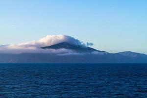 Mountain covered in fog near the ocean photo