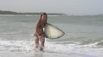 SLOW MOTION: Laughing surfer girl running out of the water