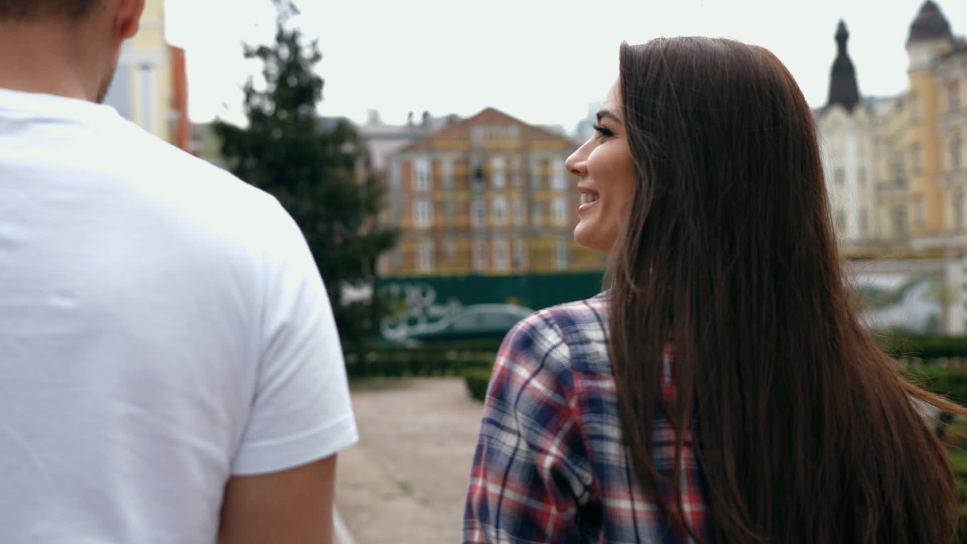 Attractive young man in white t-shirt and brunette woman on romantic date, walking holding hands, talking and happy smiling, looking at each other, back view
