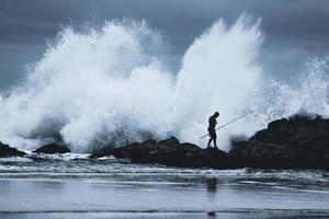 Sydney, Australia, 2020 - Silhouette of a man with fishing rod walking on a rocky coast photo