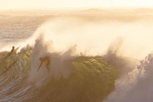 People riding a wave at golden hour photo