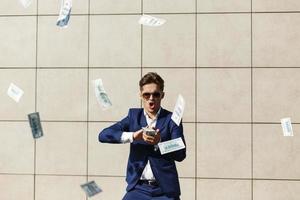 Young businessman throughs around dollars and dances on the street photo