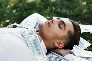 Handsome young man in a white shirt lies on the ground covered with American dollars