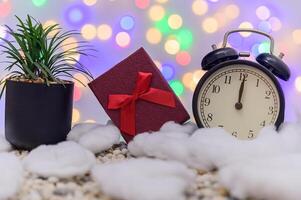 A clock, gift and a plant on a table with a christmas tree photo