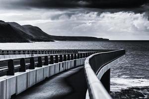 Grayscale photo of a bridge over the ocean