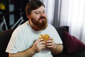 Man eats a hamburger while watching TV photo