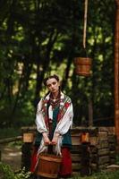 Young girl in a Ukrainian dress poses with a bucket near the well photo