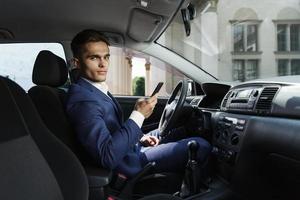 sonriente empresario se sienta dentro del coche y trabaja con su teléfono inteligente foto