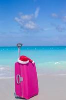 Pink suitcase with a santa claus hat on a beach photo