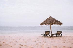 Two lounge chairs and an umbrella at a beach photo