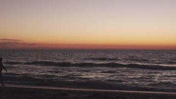 Ein älteres Ehepaar geht bei Sonnenuntergang am Strand spazieren video