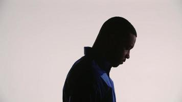 Silhouette of a young black man tilting his head down turning to the right seeing to the camera video
