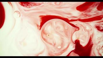 Red paint moving on white paint surface creating organic shapes in 4K video