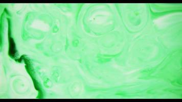 Green paint moving on white paint creating a texture of swirls and circles in 4K video