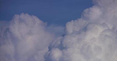 Time lapse of white giant cumulus clouds moving fast with a dark cloud in foreground in 4K video