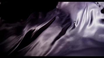 Dark purple fabric moved by the wind emerging from the darkness moving as a metallic fluid in 4K video