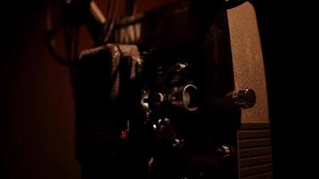 Three quaerter view of a close up of 8mm movie projector working and flashing with film reels spinning in 4K video