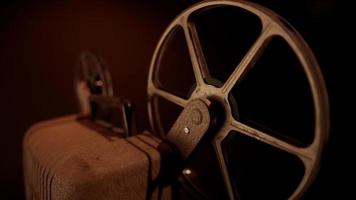 Detail of three quarter view of projector with rusty reels spinning with warm illumination in 4K video