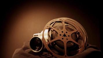 Clip de dos rollos de película girando y una vieja cámara con luz cenital y apariencia de color sepia en 4k video