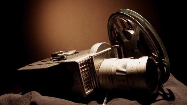 Close up of two film reels spinning and a classic camera on black