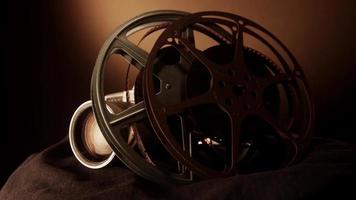 Close up of two film reels spinning beside a classic camera on black fabric with warm light on background in 4K video