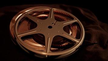 Film can with reel on top spinning on dark fabric with overhead illumination in 4K video