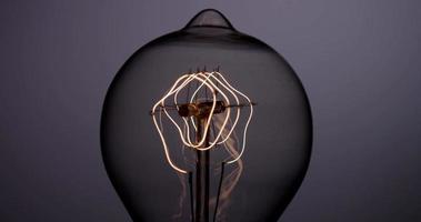 Close up front view of vintage light bulb turning on, and turning off in darkness in 4K video