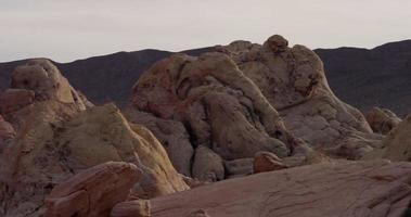 Panoramique tourné vers la gauche de roches rouges ligtht dans un paysage désertique avec des montagnes en arrière-plan en 4k video