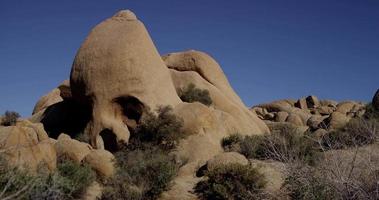  Slow panning shot of natural rock formations on desertic landscape with bushes and apiny plants in foreground in 4K video