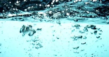 Blue scene of water splashing from right to left, then from right to left creating little bubbles in 4K video
