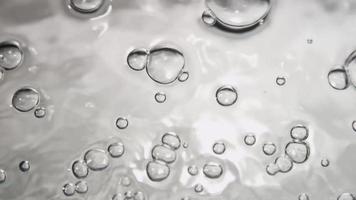 Escena monocromática de pequeñas burbujas que se fusionan y explotan en la superficie del agua en 4k