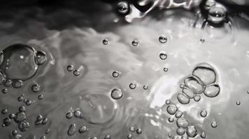 cena monocromática de padrão de bolhas dançando na superfície da água clara em 4k video