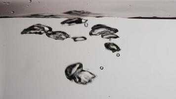 Groups of oval bubbles moving from lower section to the water surface on gray background in 4K