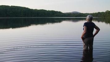 vieille dame dans le lac en regardant la forêt avec une humeur réfléchie video