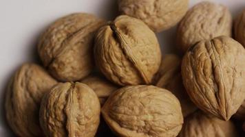 Cinematic, rotating shot of walnuts in their shells on a white surface - WALNUTS 053