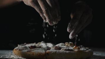 Frauenhand streut Mehl in Zeitlupe über Pizza