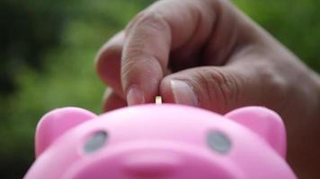 Hand putting coins in a pink piggy bank, saving money concept