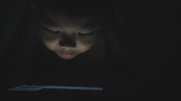 Asian little boy playing tablet or smartphone on a bed in the night video
