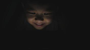 Aziatische kleine jongen die 's nachts tablet of smartphone op een bed speelt video