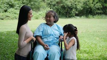 Grandmother sitting on wheelchair with daughter and granddaughter enjoy in the park together