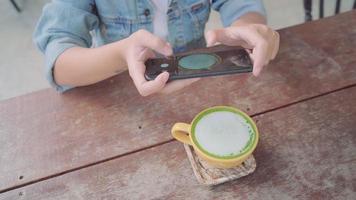 kvinnlig bloggare fotograferar grönt te kopp i café med sin telefon.