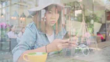 Aziatische vrouw met behulp van smartphone om te praten, lezen en sms'en zittend op tafel in café.