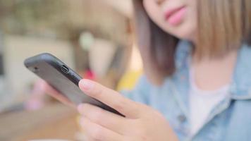 Mujer asiática que usa el teléfono inteligente para hablar, leer y enviar mensajes de texto mientras está sentado en la mesa en la cafetería. video
