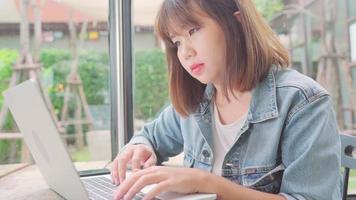affärsfrilansande asiatisk kvinna som arbetar, gör projekt och skickar e-post på bärbar dator eller dator medan du sitter på bordet i café.