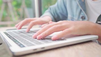 mujer asiática independiente de negocios trabajando, haciendo proyectos y enviando correos electrónicos en una computadora portátil o computadora mientras está sentada en la mesa en la cafetería. video