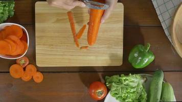 Vista superior de la mujer jefe haciendo ensalada de alimentos saludables y cortando zanahoria en la tabla de cortar en la cocina. video