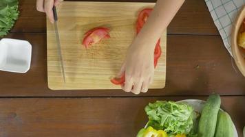 vista superior do chefe da mulher fazendo salada de alimentos saudáveis e picar tomate numa tábua na cozinha. video