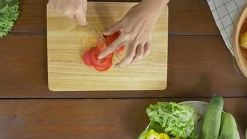 Vue de dessus du chef de femme faisant de la salade des aliments sains et hacher la tomate sur une planche à découper dans la cuisine. video