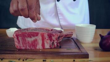 ralenti - gros plan d'un chef gastronomique ou cuisiner assaisonner un morceau de viande de bœuf frais avec du sel de mer et des poivrons épicés moulus. video